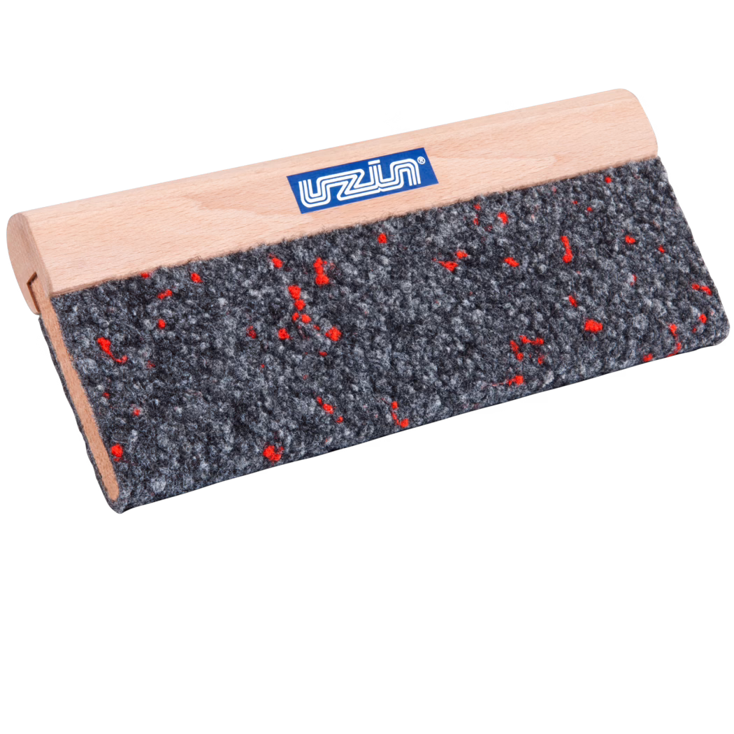 UZIN_Dummy_cork rubbing board textile covered-UZIN_2014-01 Nahaufnahme eines rechteckigen Werkzeugs mit einem glatten hellen Buchenholzgriff und einer groben grauen Filzauflage, durchsetzt mit kleinen roten Fasern; auf dem Griff ist ein kleines blaues Markenetikett sichtbar. Das Werkzeug ist schräg vor weißem Hintergrund fotografiert, wodurch die Filzstruktur und die feine Holzmaserung betont werden.